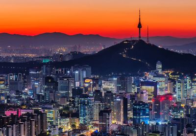 Illuminated buildings in city against sky at sunset