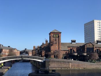 Arch bridge over river amidst buildings against clear blue sky