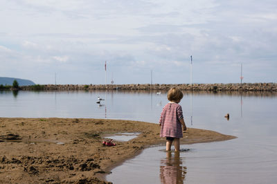 Rear view of girl standing in lake against cloudy sky