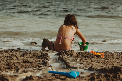 A girl sits on the beach in the sand and plays with toys. view from the back.