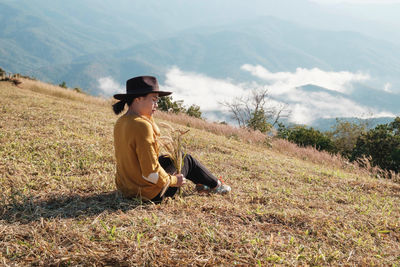 Woman sitting on grass against mountain