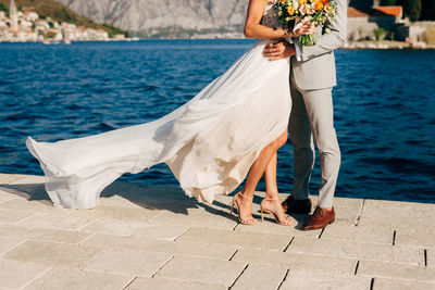 Low section of couple standing on pier by sea