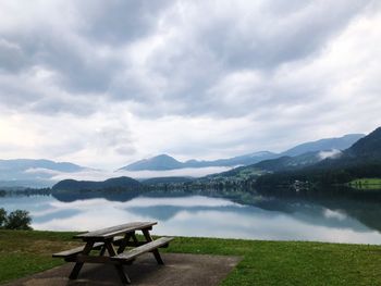 Empty bench by lake against sky