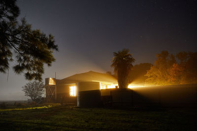 Silhouette trees and buildings on field against sky at night