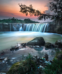Scenic view of waterfall against sky at sunset