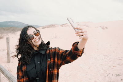 Portrait of young woman wearing sunglasses standing at beach
