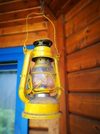 Close-up of yellow oil lamp hanging against wooden wall