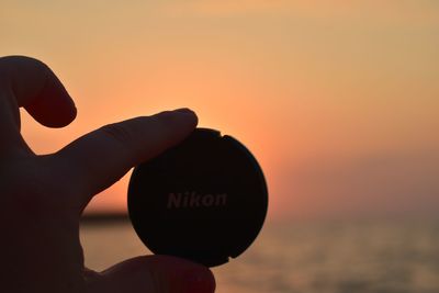 Close-up of hand holding plastic container against sky during sunset