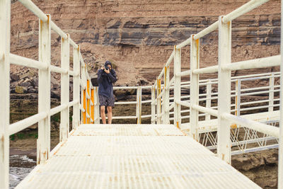 Man photographing while standing on footbridge at beach