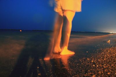 Low section of person standing on beach against sky during sunset