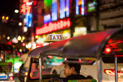 Reflection of man on illuminated car in city at night