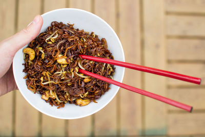 Cropped image of person holding noodles bowl with chopsticks over table