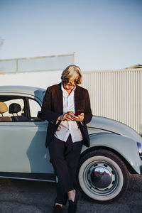 Senior man standing in front of vintage car using mobile phone