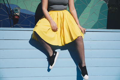 Low section of young woman sitting on bench against mosaic wall