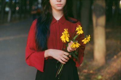 Midsection of woman holding yellow flowers while standing on road