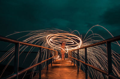 Person spinning wire wool on footbridge at night