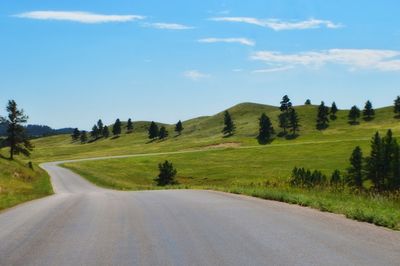 Road amidst trees and landscape against sky