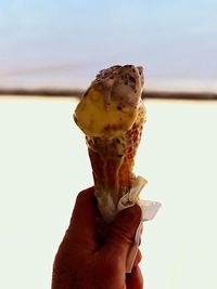 Close-up of hand holding ice cream against sky