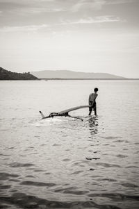 Rear view of shirtless man with windsurfing board in sea