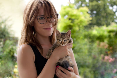 Portrait of woman holding kitten against trees