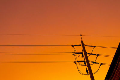 Low angle view of silhouette electricity pylon against orange sky