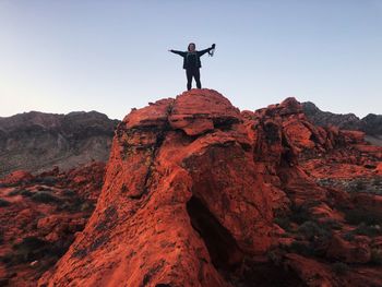 Low angle view at sunrise of womman standing on rock holding camera 