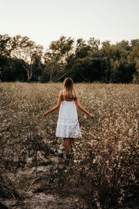 Rear view of woman with arms raised on field against sky