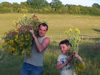 Portrait of father with son carrying flowers on shoulders while standing at farm