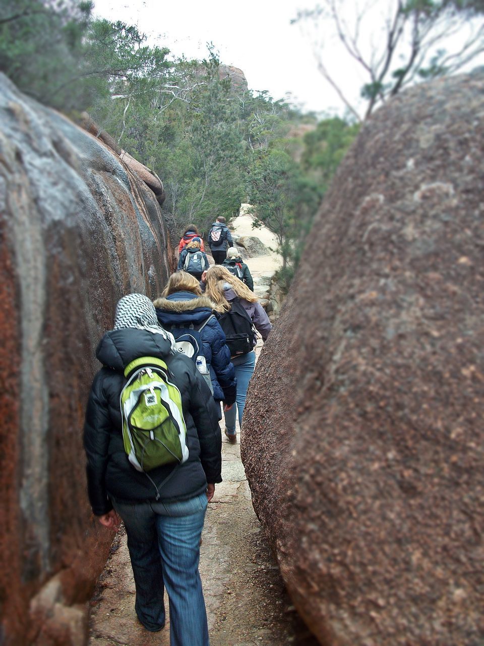 REAR VIEW OF MAN STANDING ON ROCK AGAINST MOUNTAIN