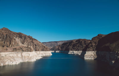 Scenic view of reservoir amidst mountains against clear blue sky