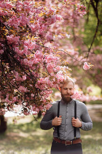 Man with suspenders standing near cherry blossom tree