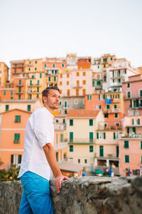 Young man standing against buildings in city against sky