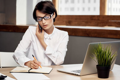 Young woman using phone while sitting on table