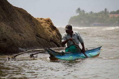 Man rowing boat in sea against sky