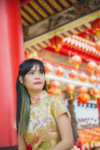 Asian woman wearing traditional yellow cheongsam qipao dress sitting and looking away 