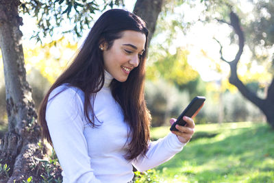 Young woman using phone while standing on plant