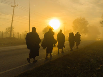 Silhouette people walking on road against sky during sunset