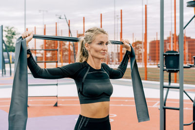 Young athletic woman is training on the sports ground using sports elastic bands.