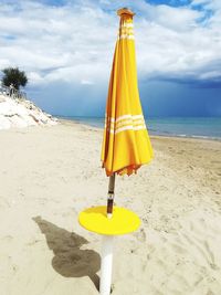 Close-up of yellow umbrella on beach against sky