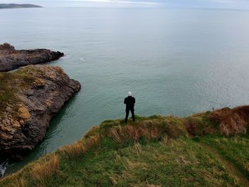 Rear view of man standing on cliff by sea