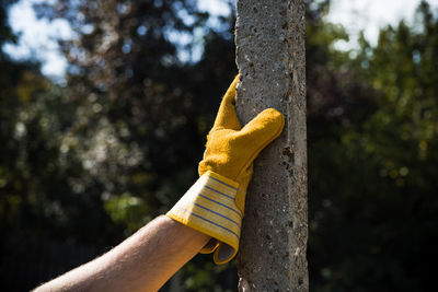 Close-up of hand with glove touching concrete pole outdoors