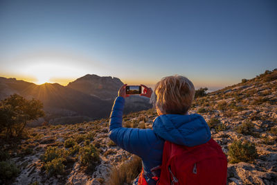 Woman hiking and taking a picture of the puig campana mountain.