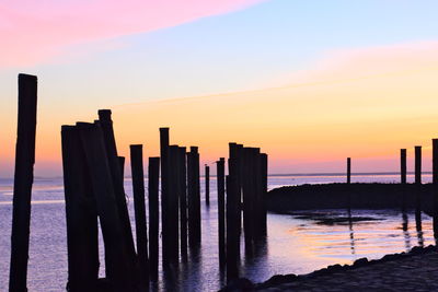 Silhouette wooden posts on beach against sky during sunset