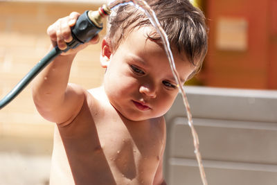 Happy little boy playing with water hose in the backyard