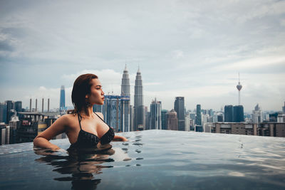Beautiful young woman in swimming pool looking at cityscape