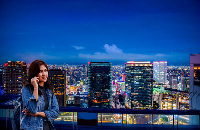 Full length of man photographing illuminated city buildings against blue sky