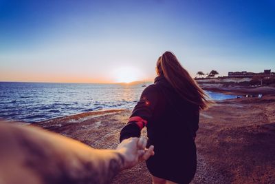 Cropped image of man holding woman hand at beach during sunset