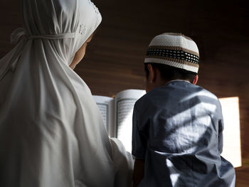 Rear view of sibling reading koran at home