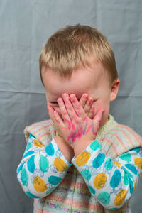 Close-up of boy with messy hands covering face by curtain