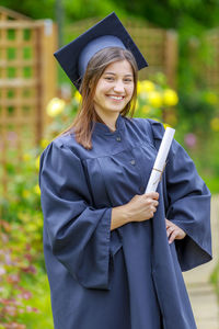 Portrait of young woman in graduation gown standing at park